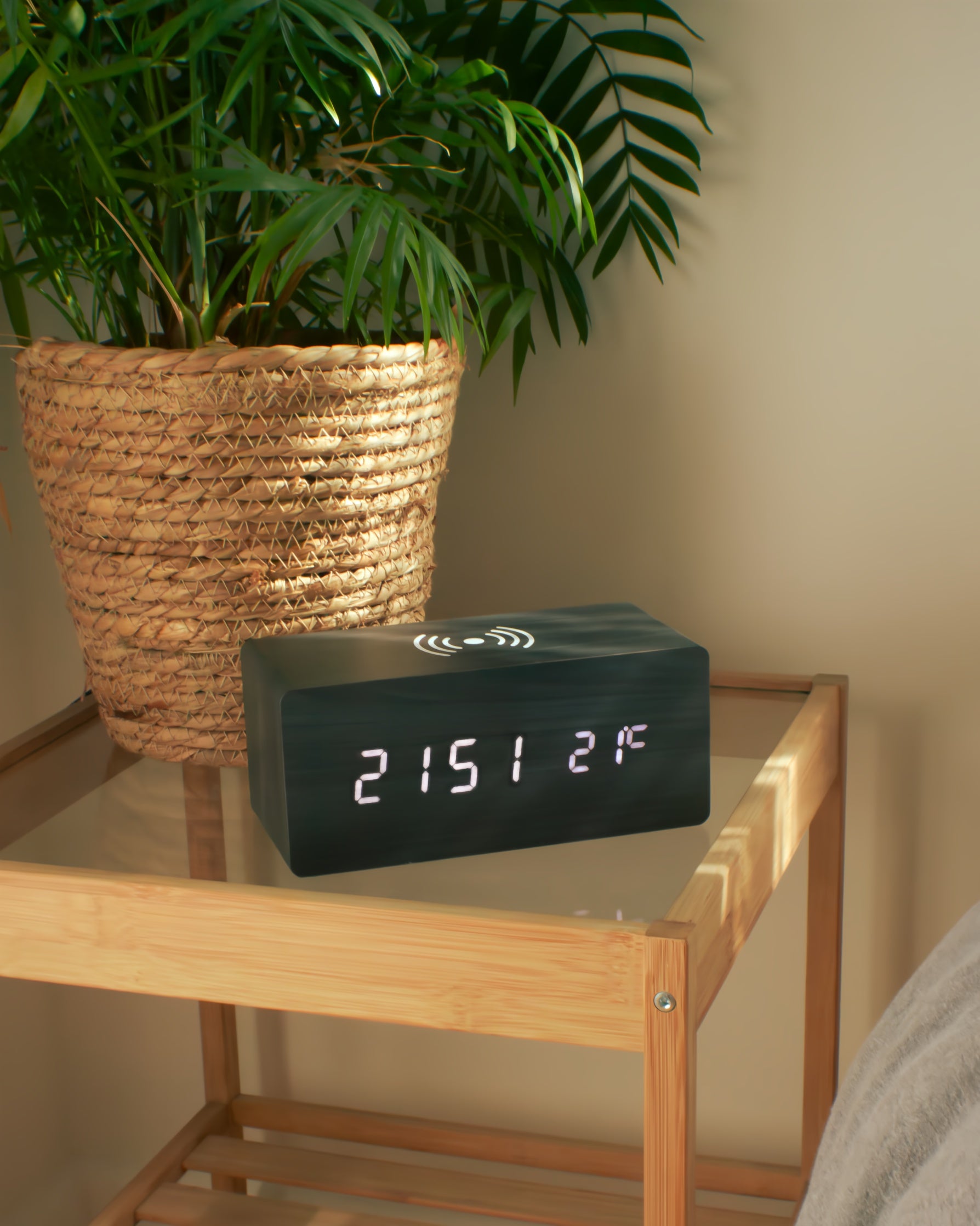 Digital clock on a wooden shelf with a plant in the background